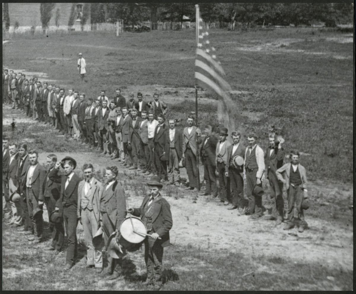 Regiment oppstilt på rekke med amerikansk flagg og trommeslager, historisk svart-hvitt-foto